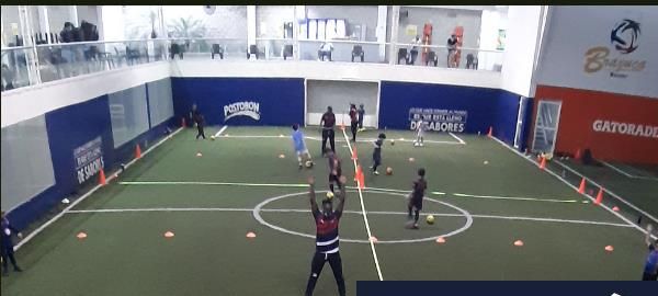 Niños entrenando con conos en cancha sintética